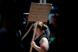 A woman holds a cardboard sign directed at Premier Peter Malinauaskas