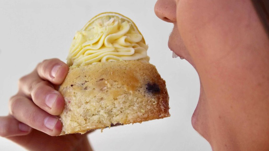 A woman with an open mouth is about to take a bite from a muffin with piped cream and lemon on top