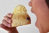 A woman with an open mouth is about to take a bite from a muffin with piped cream and lemon on top