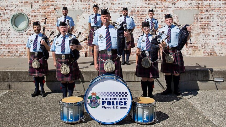A pipes and drums band standing in front of a wall in Brisbane.