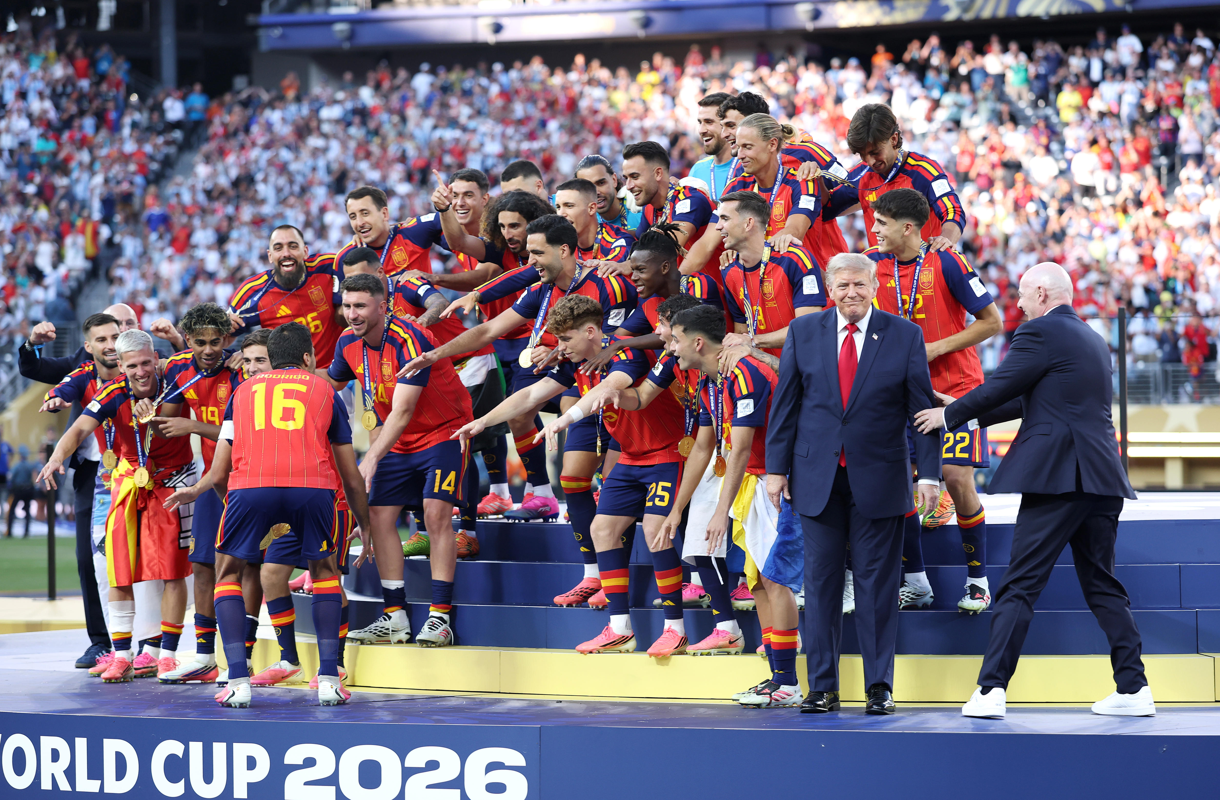 A male soccer team celebrates as a man in a suit is led off to one side.