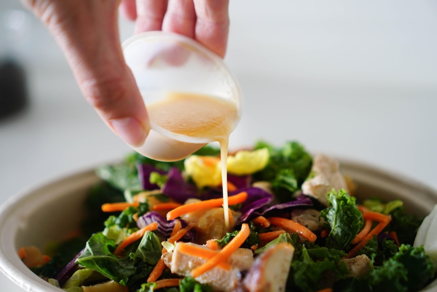 Close-Up Photo of a Person Pouring Salad Dressing into Vegetables