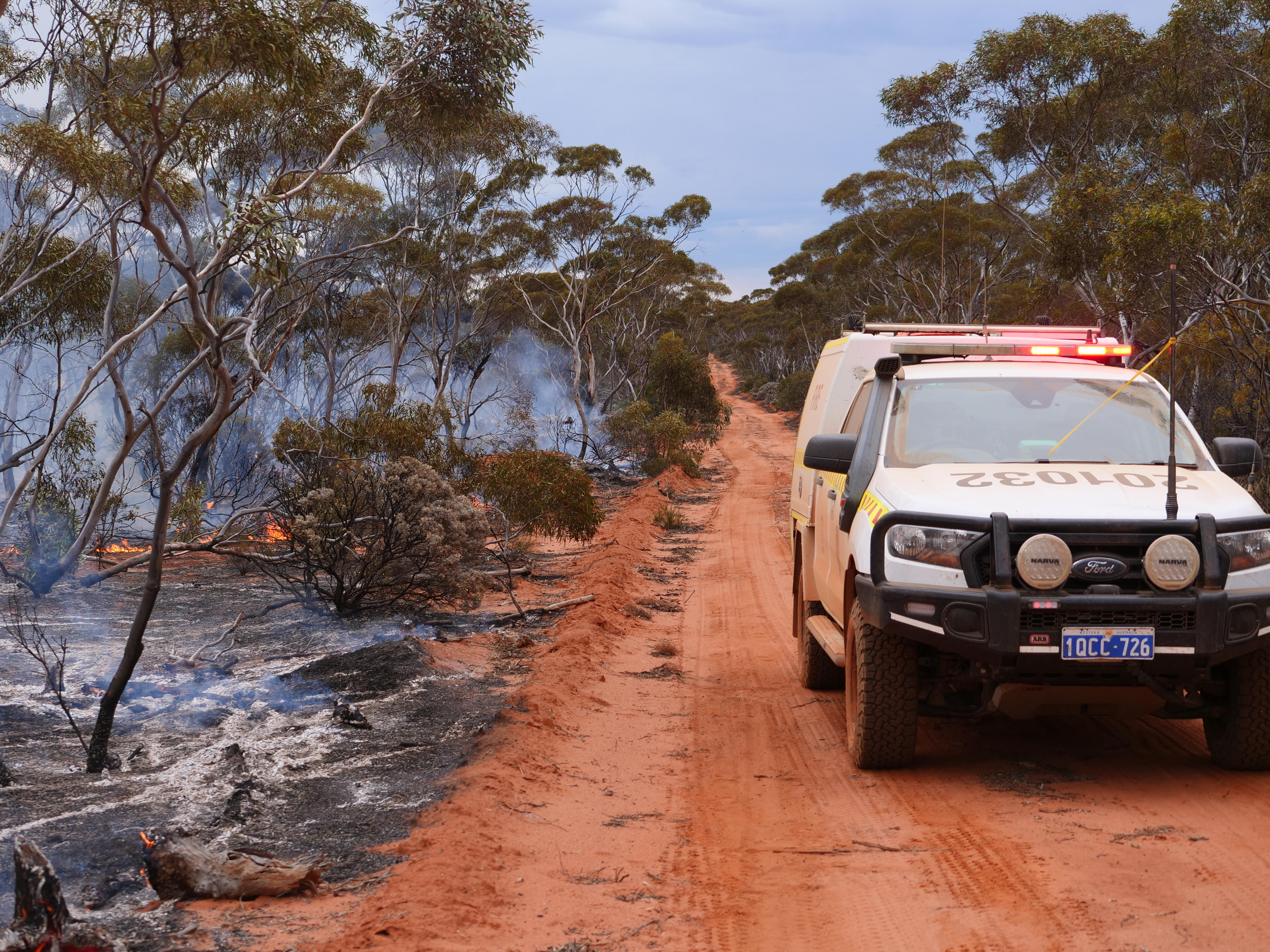 A fire vehicle drives along an outback track on the border of a bushfire