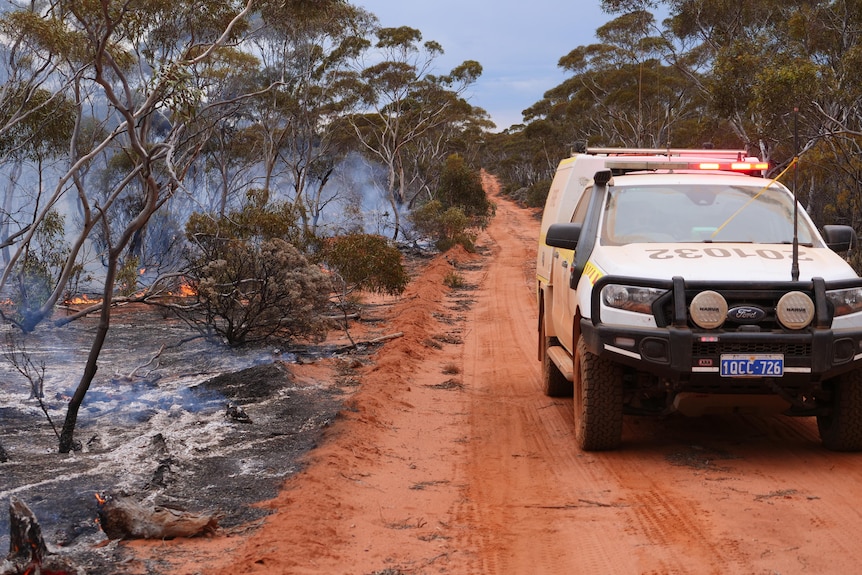 A fire vehicle drives along an outback track on the border of a bushfire.