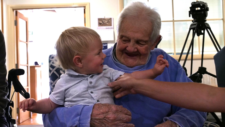 a toddler in a button-up shirt smiles at an old man