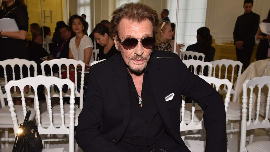 French rock singer Johnny Hallyday sits on a chair looking at the camera at a fashion show
