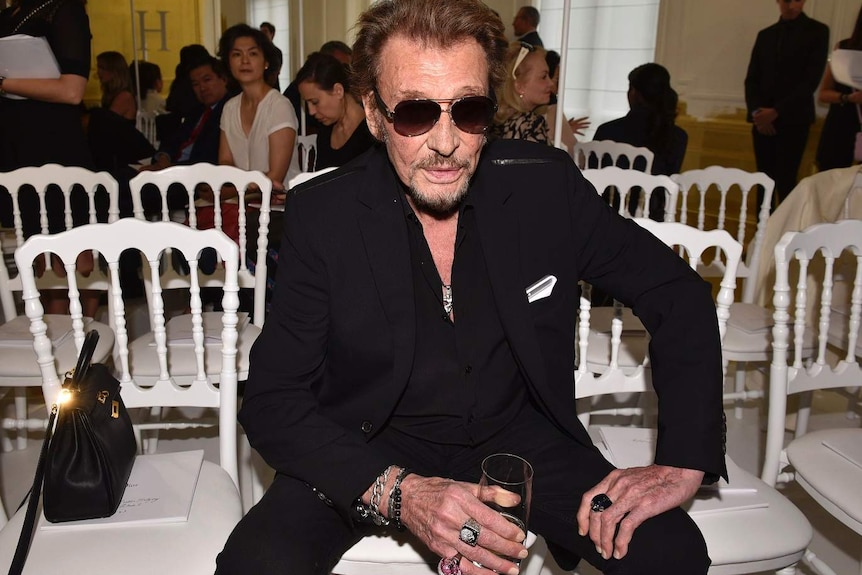 French rock singer Johnny Hallyday sits on a chair looking at the camera at a fashion show