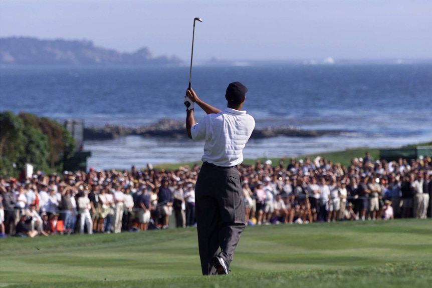 A rear view of a golfer at the end of his backswing at the US Open in front of the Pacific Ocean.
