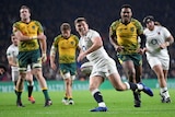 a rugby player in a white smiles as he runs in to score as players in gold jerseys look on