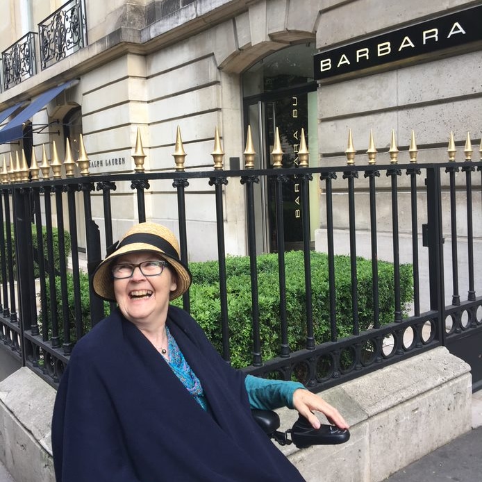 A woman in a wheelchair wearing a straw hat and smiling