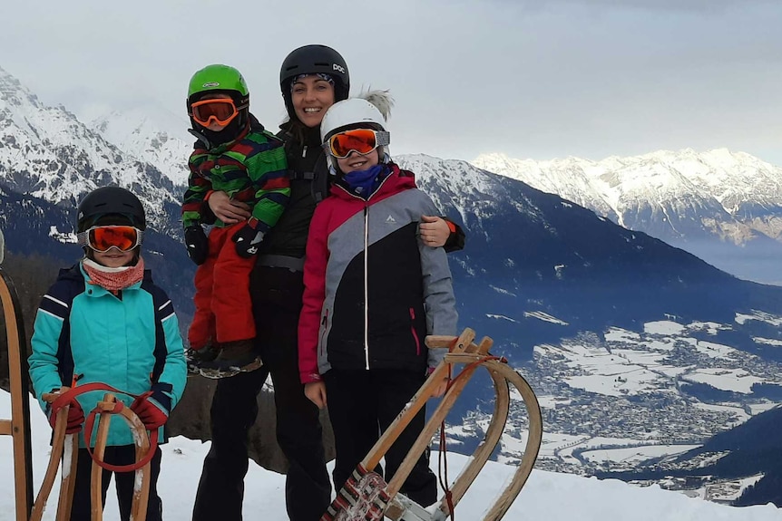 A moth poses with her three children in snow gear with sleds