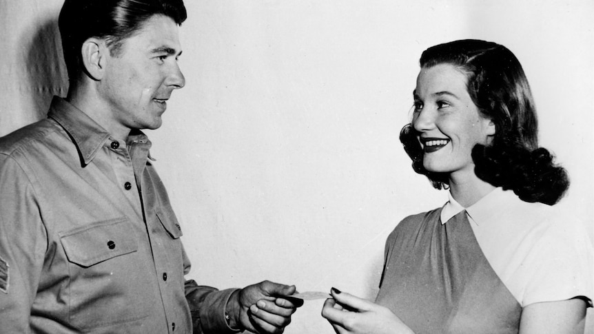 A black and white image of Ronald Reagan handing a woman a union card. 