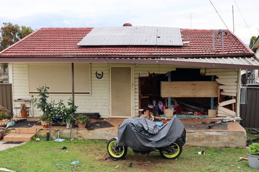A motorbike outside a house with a hole in the front where a car went through