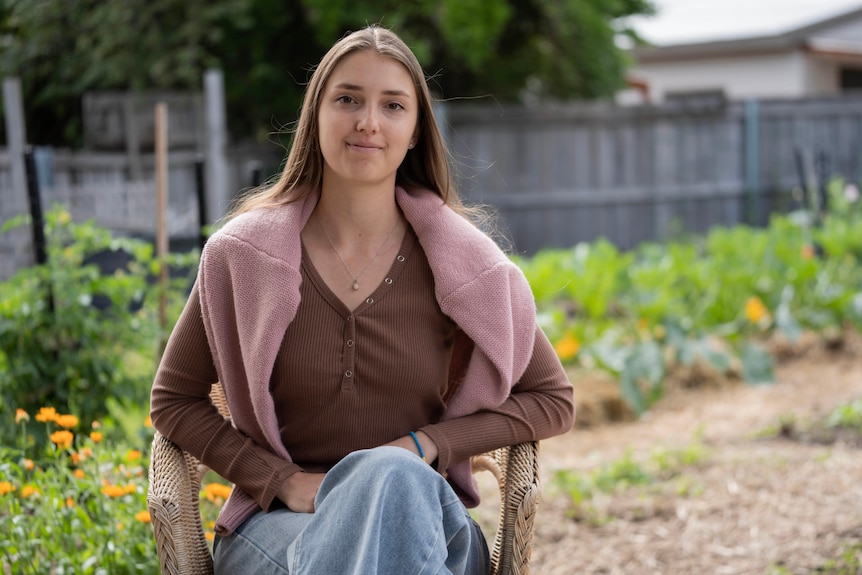 A young woman with long brown hair sits in a garden