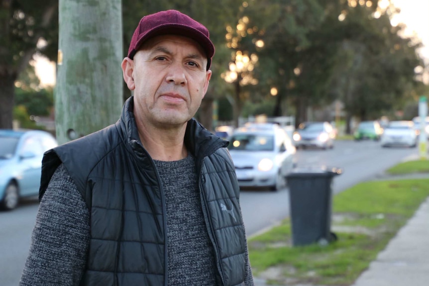 Hamid Hafid wearing a purple hat, standing on the side of Orrong Road with traffic passing behind him.
