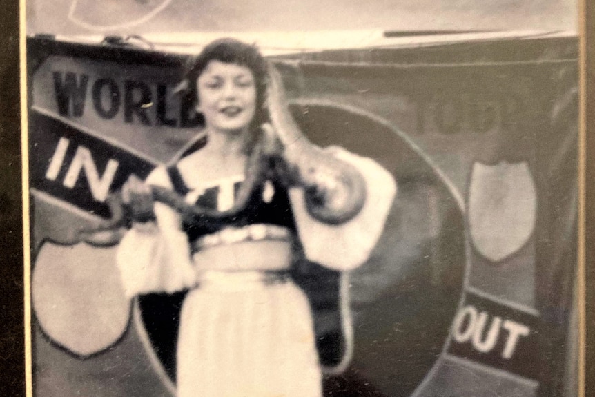 A black and white photo of a woman in a white dress with a snake around her arms and neck.