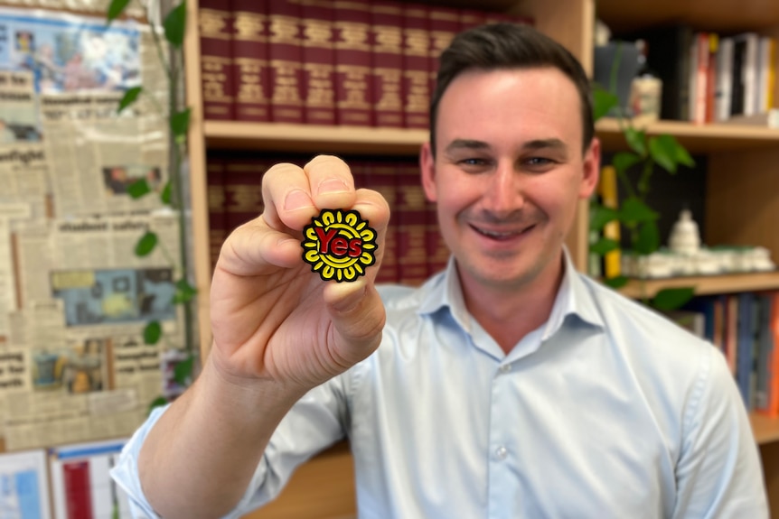 Sam O'Connor holds a Yes badge in front of a bookcase.