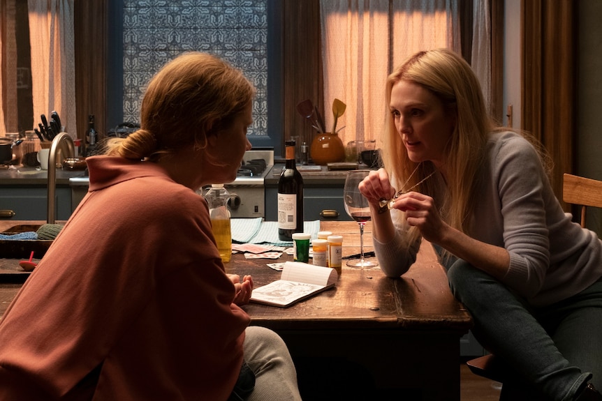 Film still of Julianne Moore as Jane leaning in to talk to Amy Adams as Anna at a table with wine in The Woman in the Window