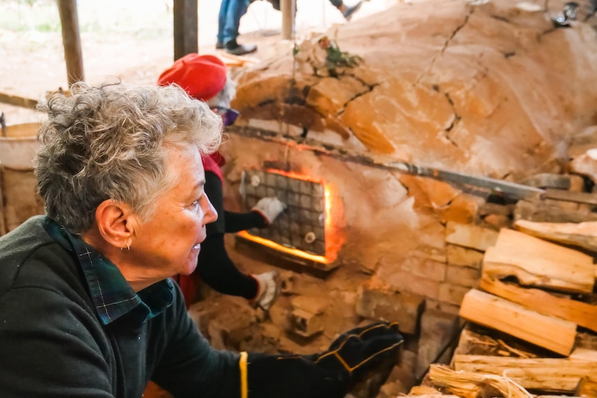 Two women work at a wood fired kiln