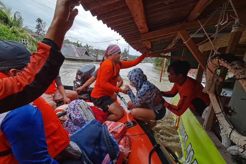 Ratownicy w jaskrawo pomarańczowym zestawie pomagają ludziom uwięzionym w zalanych domach na gumowej łodzi.