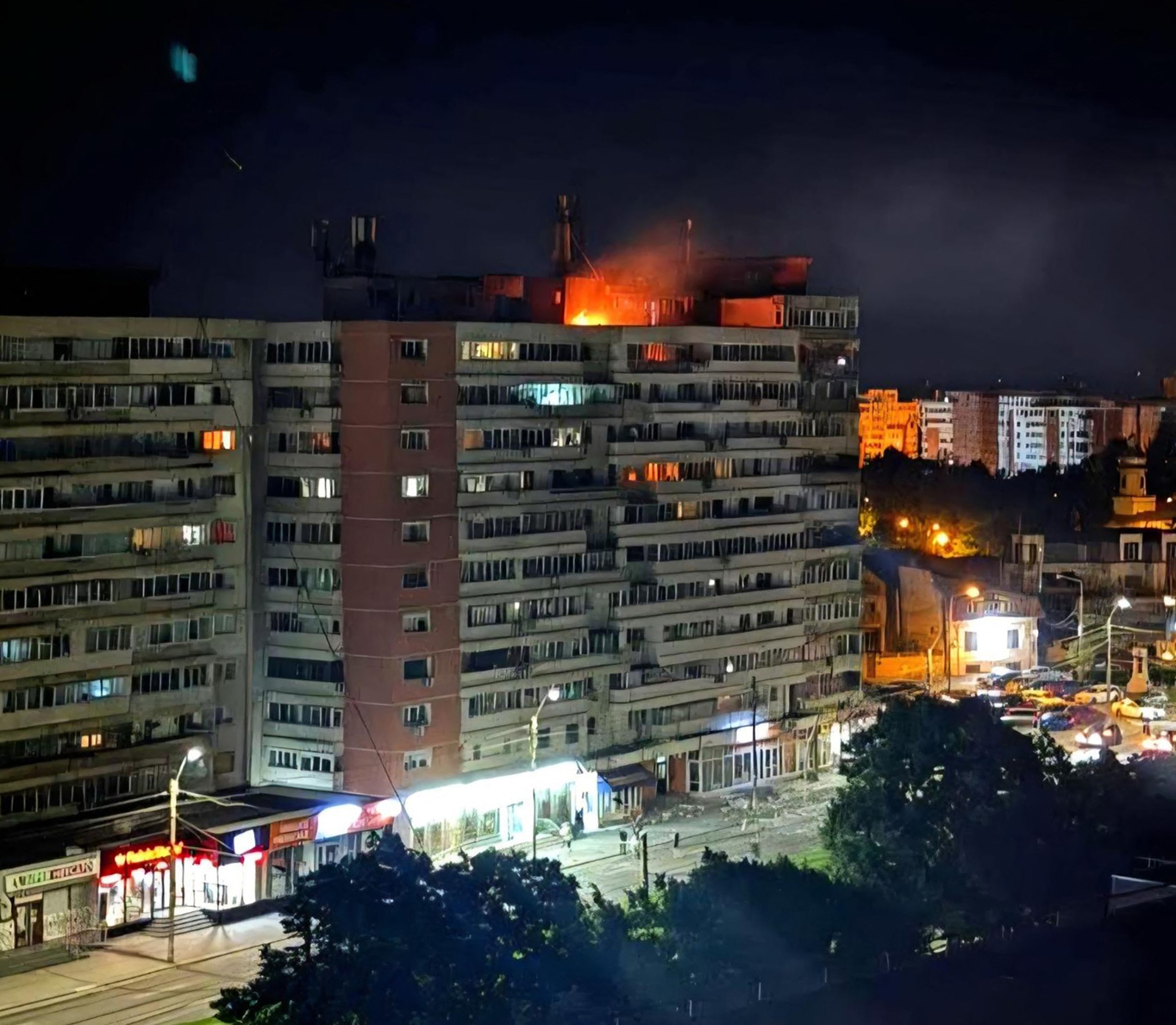 Un bloque de viviendas de noche, el tejado ardiendo tras un impacto