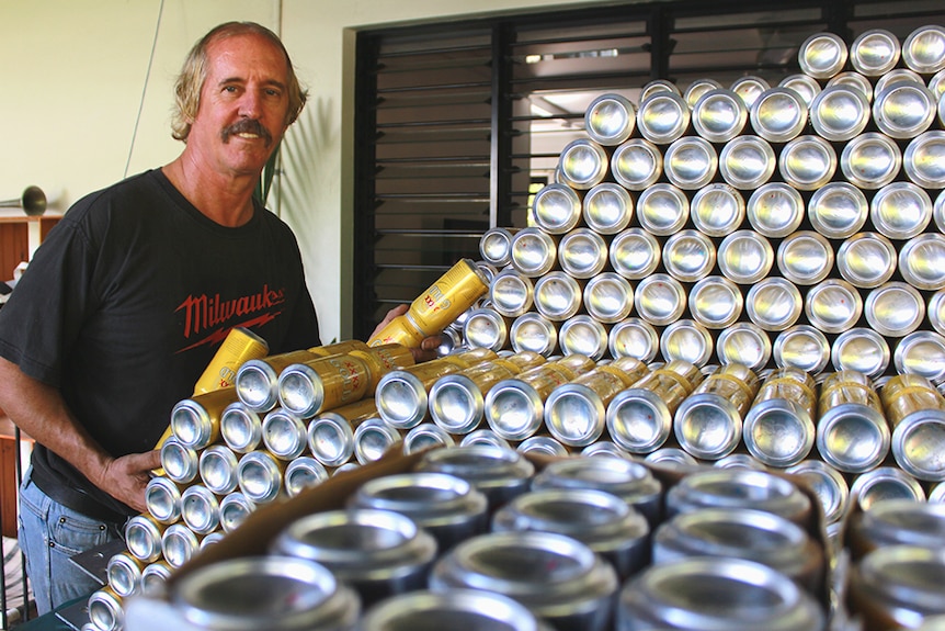 Beer can boat builder Mick Keeley stands next to a pile of beer cans