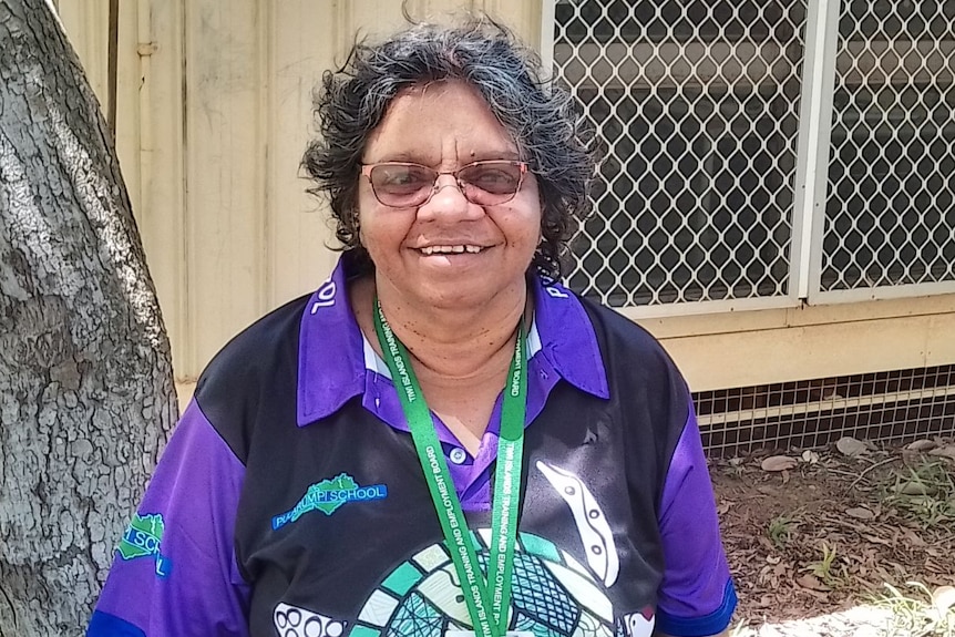Indigenous woman with glasses smiles at camera with lanyard around neck