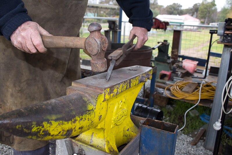 Hands hammering a piece of metal on a yellow anvil