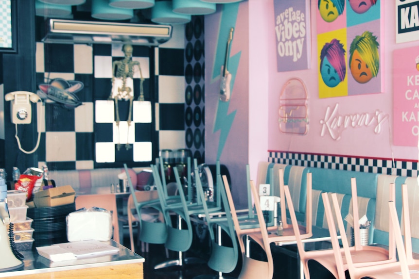 Through the window of Karen's Diner with pink and blue chairs stacked up, no one inside