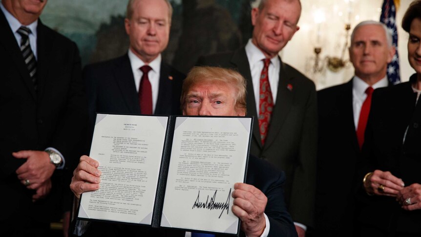 President Donald Trump displays signs a presidential memorandum imposing tariffs and investment restrictions on China.