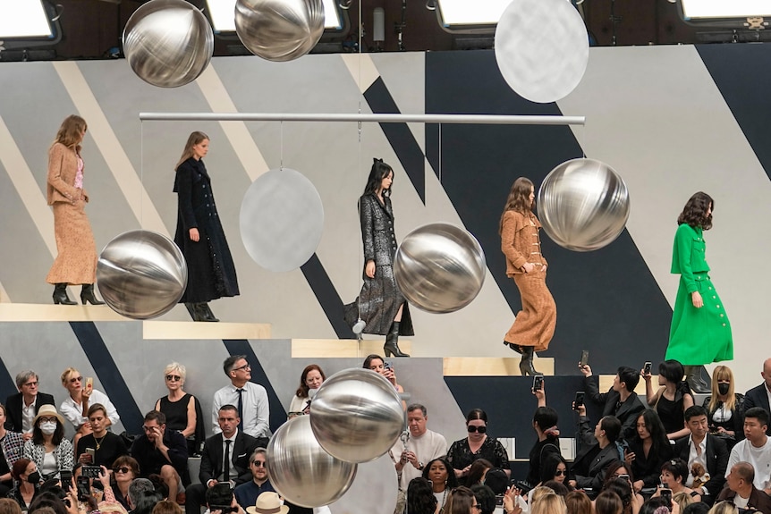 Five models walking down a floating staircase over onlookers. 