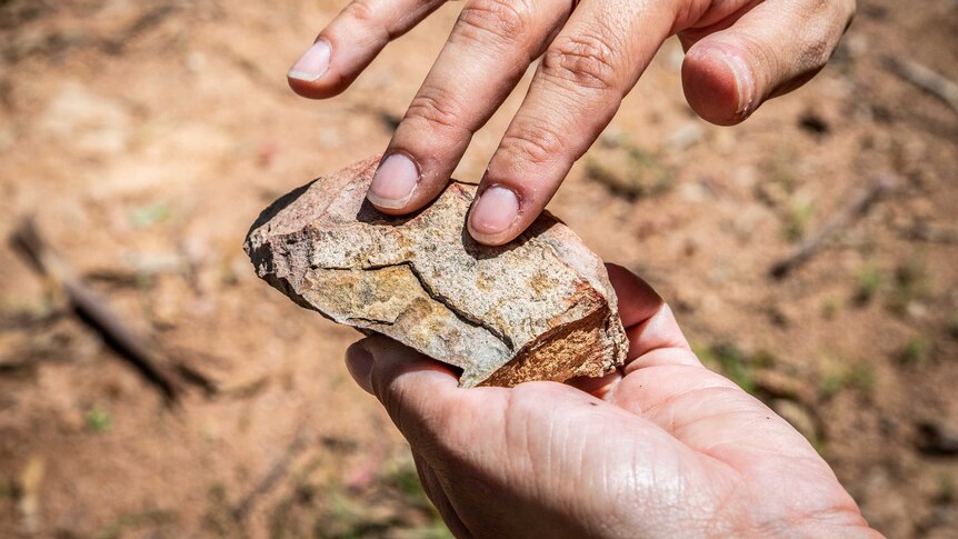 A woman holds her fingers into a specific position on a rock as to indicate how it might have been used by ancestors.