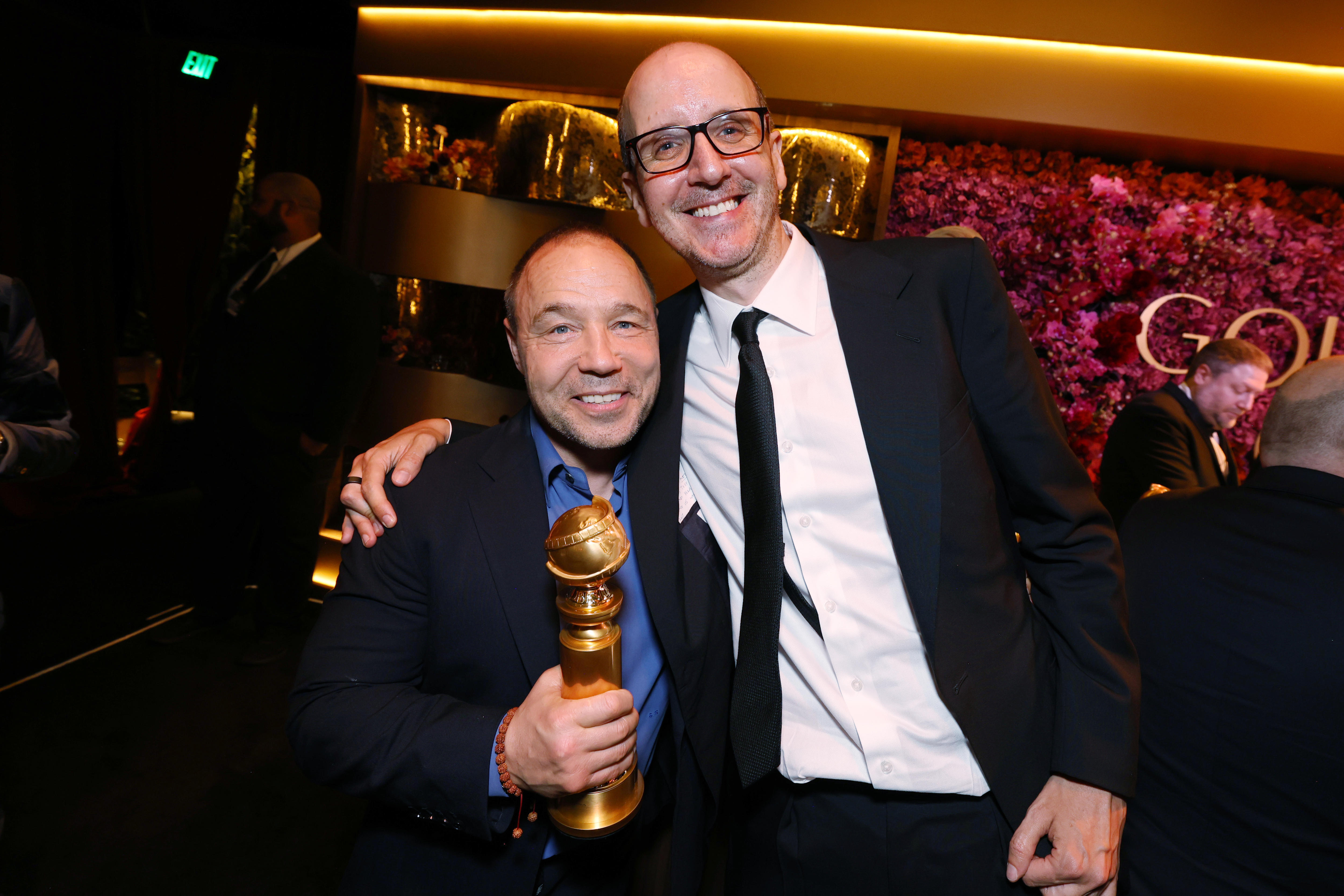 Jack Thorne, de 47 años, con gafas, vestido de traje, sonriendo, con el brazo alrededor de Stephen Graham, de 52 años, que sonríe y sostiene un Globo de Oro en la mano.