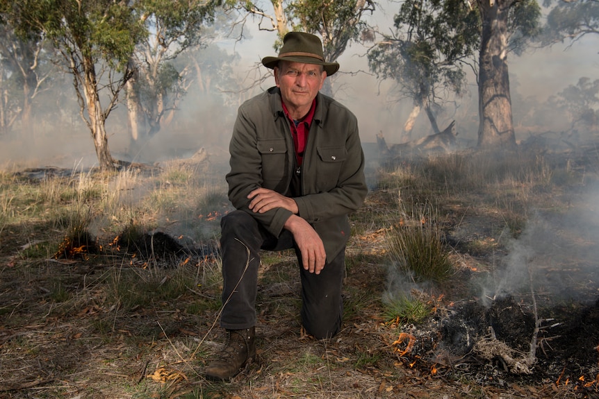 Man kneels looking at camera, smoke around him.