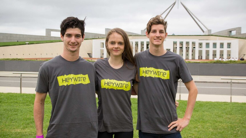 Three students stand in front of Parliament House in Canberra