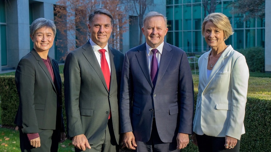 Two women and two men pose for a photograph in front of a building.