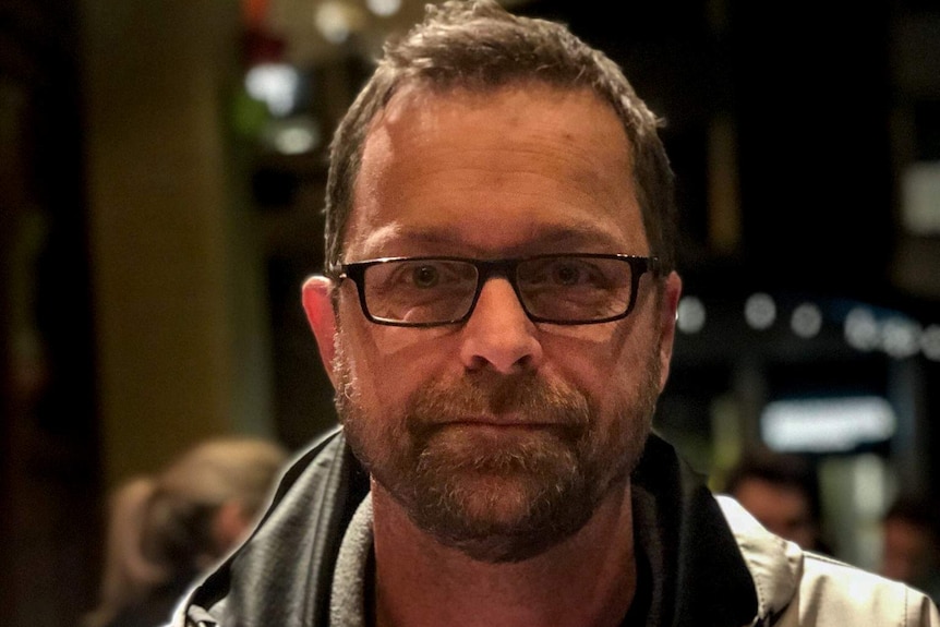 Todd Johnson, wearing glasses and a jacket with brown hair and facial hair, sitting in a restaurant.