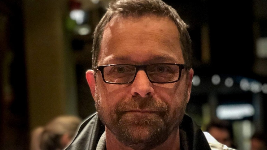 Todd Johnson, wearing glasses and a jacket with brown hair and facial hair, sitting in a restaurant.