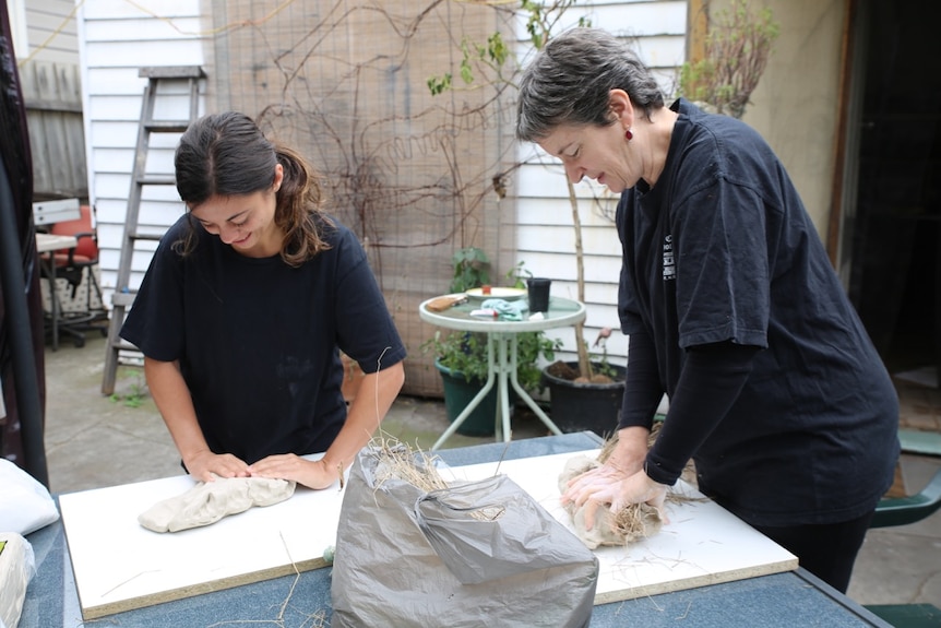 Two women standing at a table make traditional hats.