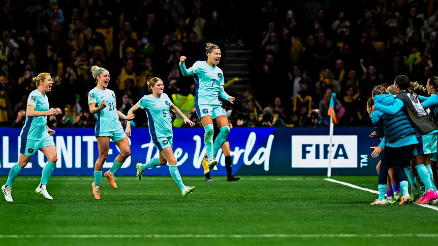 A women's soccer team wearing light blue uniforms runs to the sideline celebrating