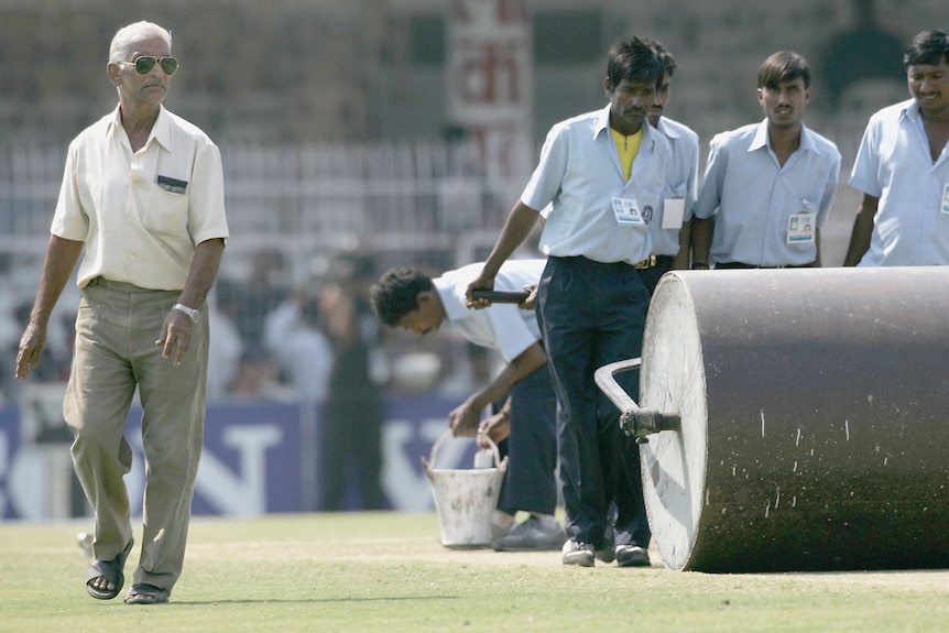 Kishor Pradhan walks nest to a large roller being tended to by three men in shirts