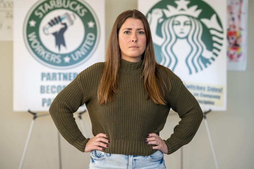 A woman wearing a green shirt stands in front of a Starbucks sign with her hands on her hips.
