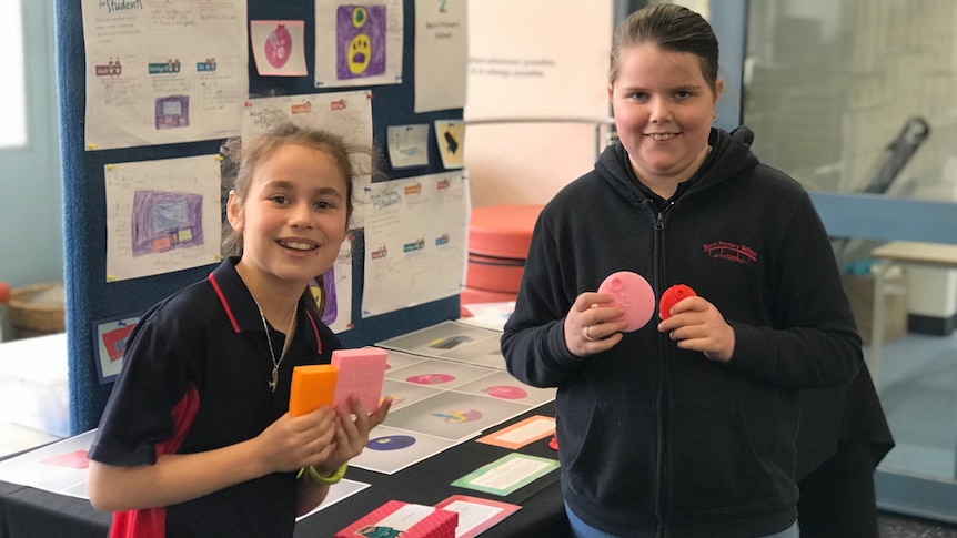 Two girls smiling at the camera holding 3D printed products