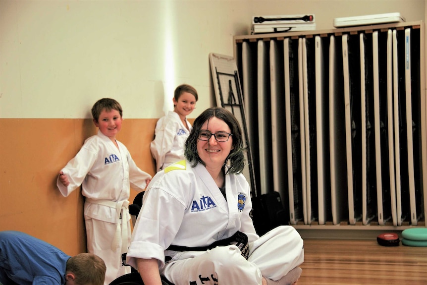 Taekwon-Do instructor Nicola Harrod sits smiling in her class with two of her students smiling in the background.