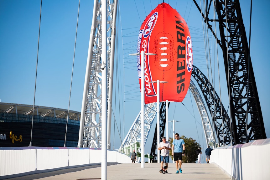 Two men walking over a bridge with a giant inflatable football overhead.
