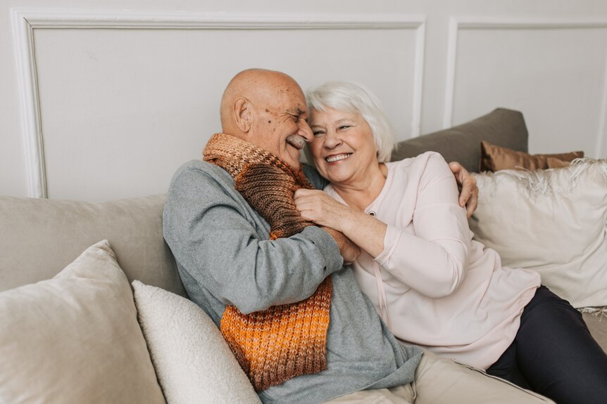 An older man and woman cuddling and laughing on a beige sofa
