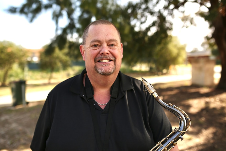 Andrew Fairbairn smiling and holding his saxaphone.