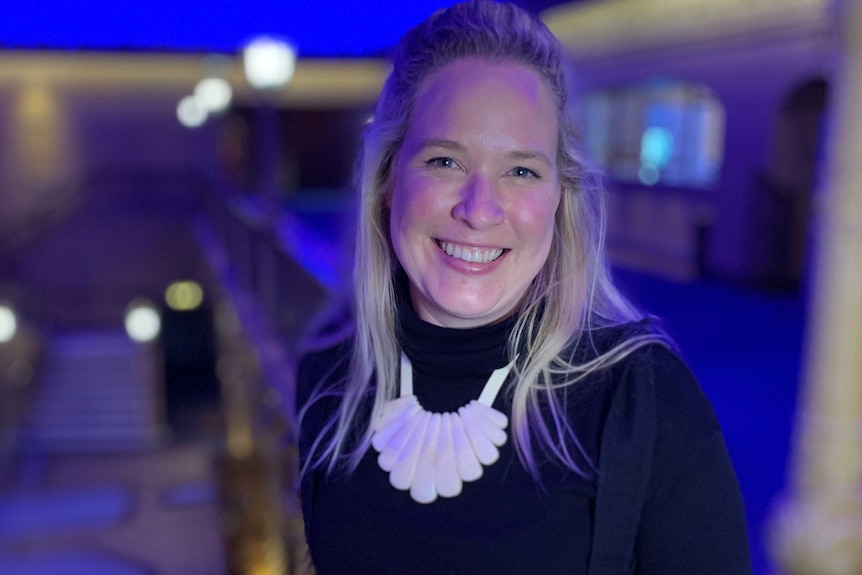 Sally Mather, standing inside the Forum Theatre, looks at the camera smiling.