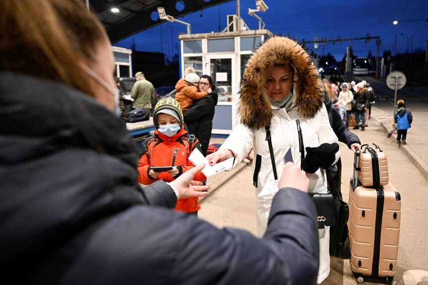 A woman and child with bags and suitcases hand documents over to an official at the Ukraine-Slovakia border crossing.