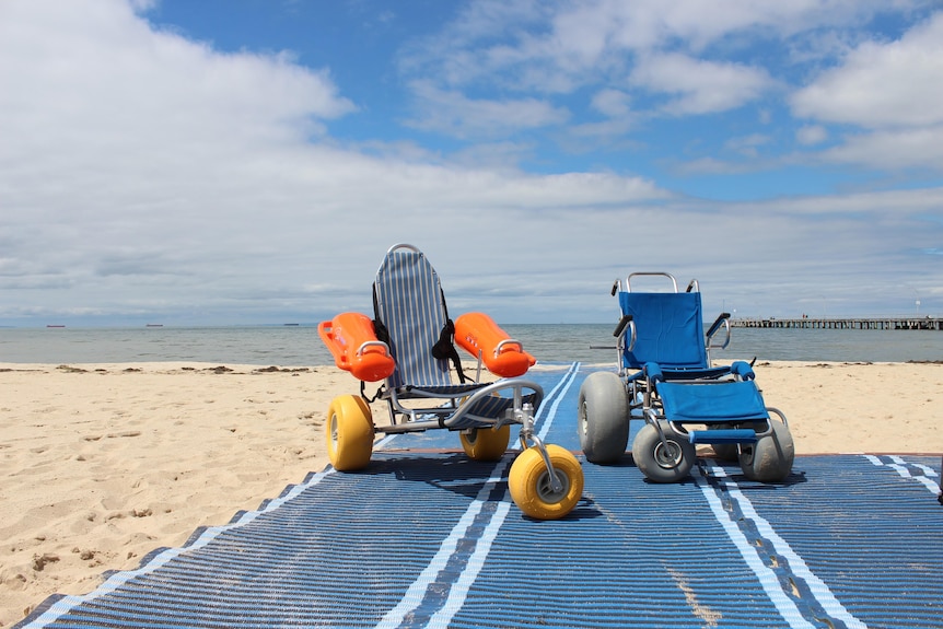 Two wheelchairs sit on blue mats on a beach